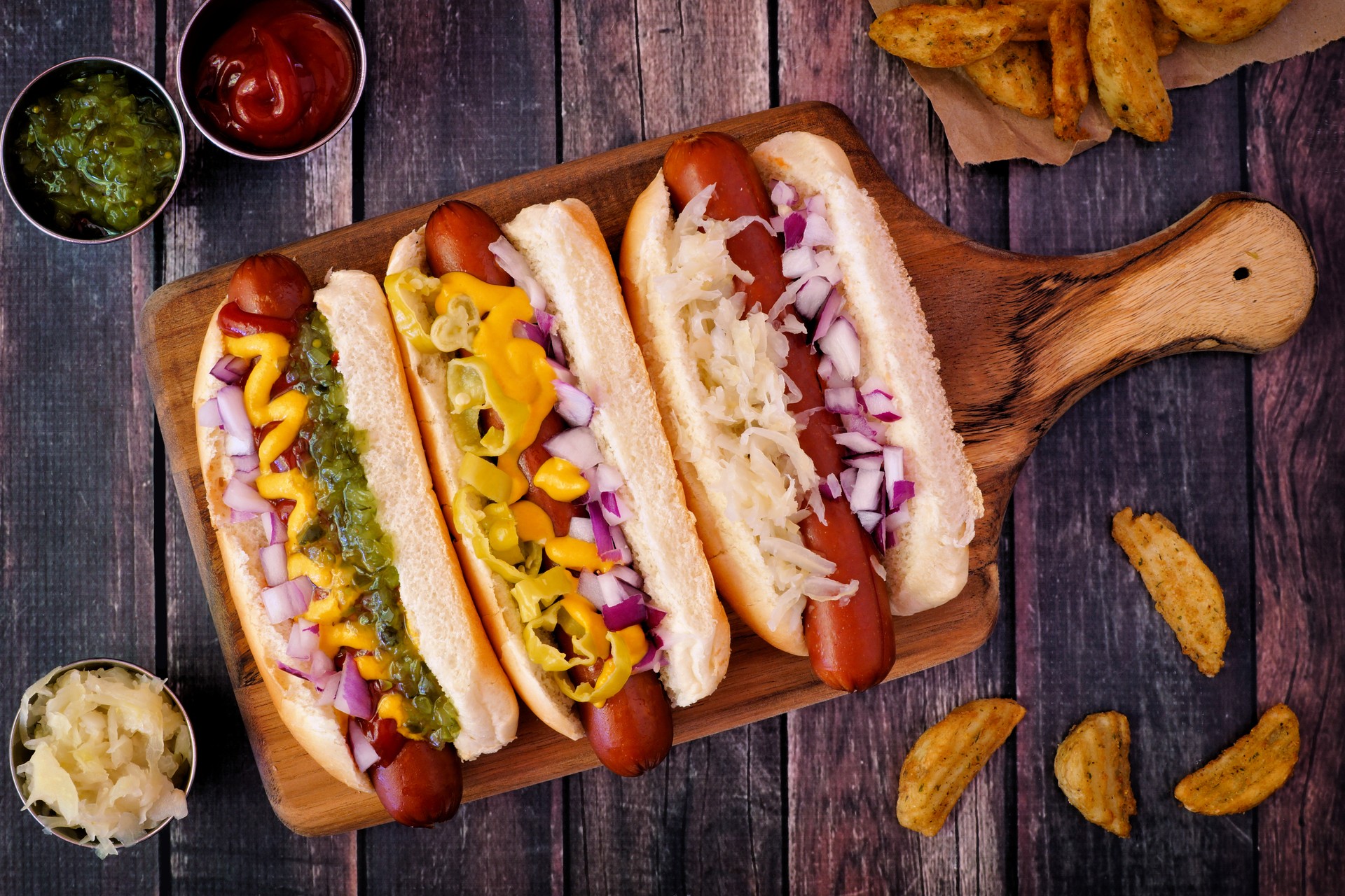 Hot dogs with assorted toppings on a paddle board, overhead scene