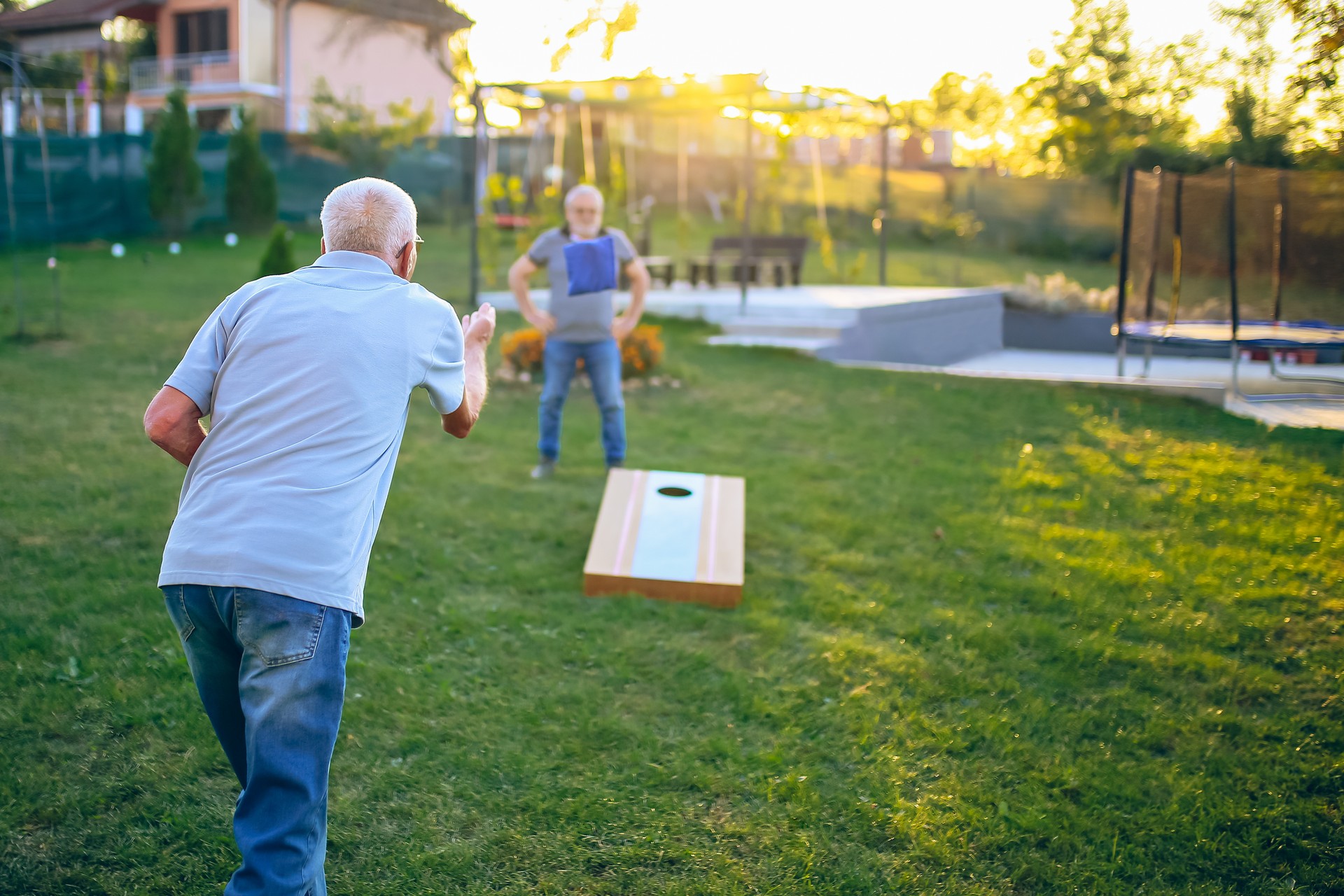 Two old friend play corn hole in backyard